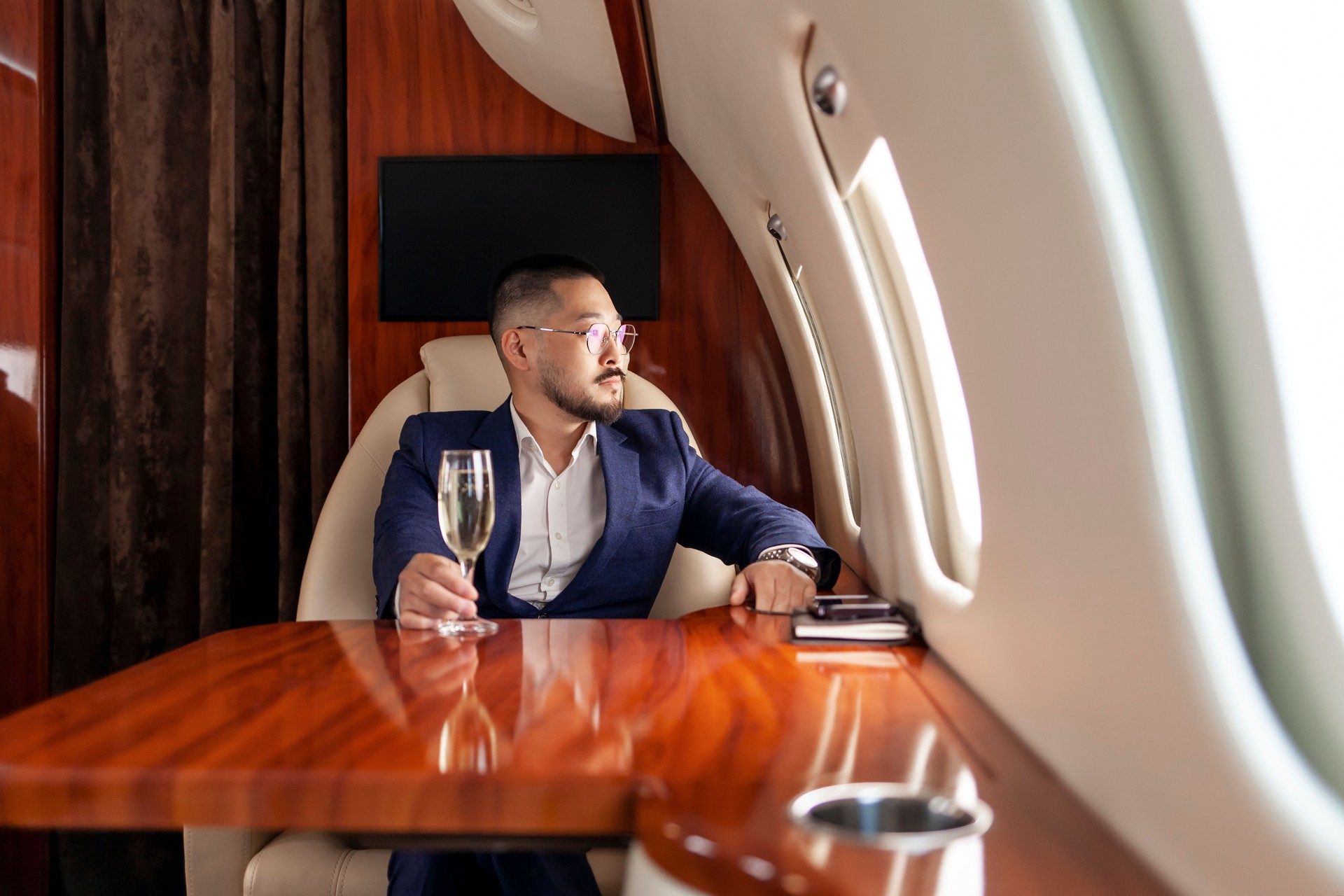 asian businessman in suit and glasses with glass of champagne flies in private luxury jet, korean entrepreneur